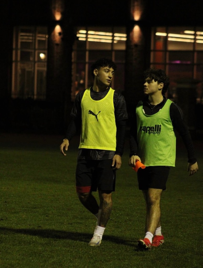Two soccer players in training bibs walking off the pitch under the lights