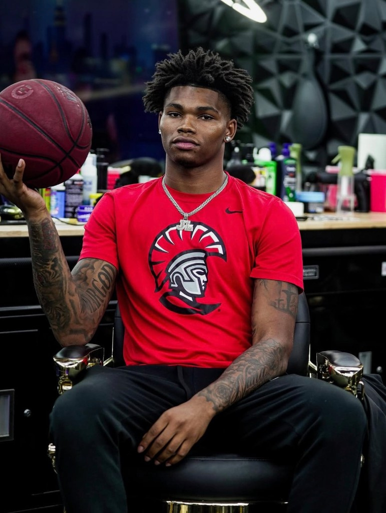 Athlete in a red shirt holding a basketball in a barber chair